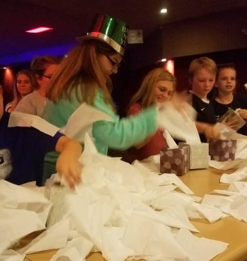 A group of children joyfully playing with crumpled paper towels in a bright, colorful room.