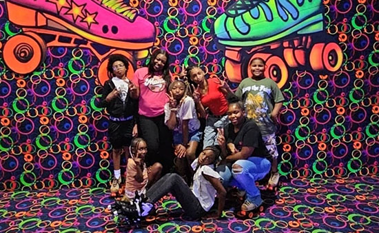 A group of children and teens poses playfully in front of a vibrant roller skating-themed backdrop with colorful patterns.